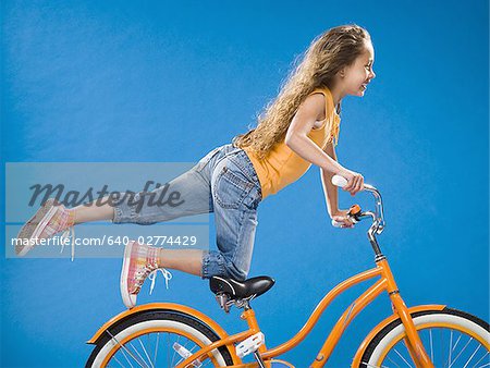 Girl on orange bicycle kneeling on seat with foot up