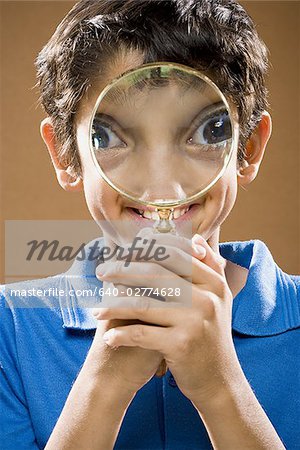 Boy holding magnifying glass to face smiling