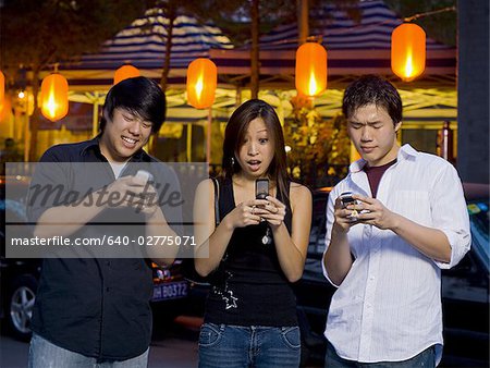 Three people with cell phones outdoors at night smiling
