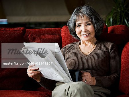 senior woman reading a newspaper on the couch