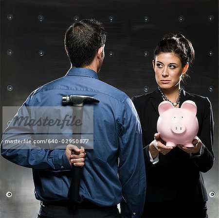woman holding a piggy bank and a man holding a hammer behind his back