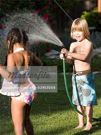 little boy spraying a little girl with the hose