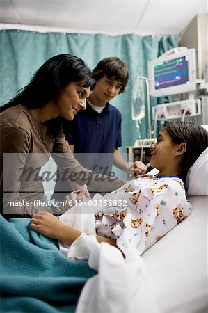 Mother and son talking to girl in hospital bed