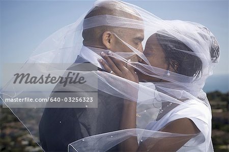 Profile of a newlywed couple kissing each other under a veil