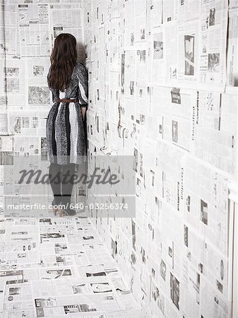 Young woman standing in corner of room covered with newspapers