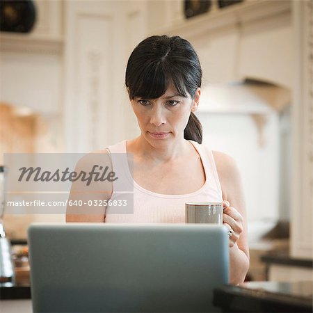 USA, Utah, Alpine, mid adult woman standing near laptop and holding mug