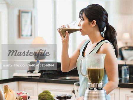 USA, Utah, Alpine, mid adult woman standing in kitchen and drinking cocktail