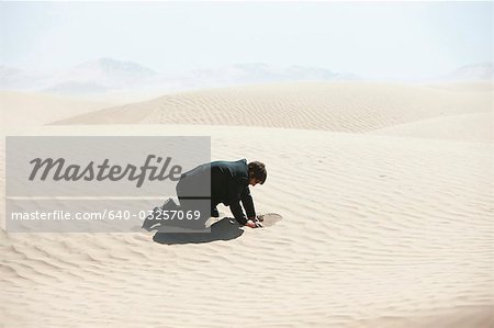 USA, Utah, Little Sahara, mid adult businessman digging hole on desert