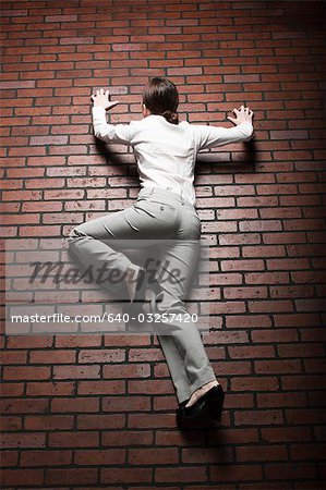 Studio shot of young woman climbing up brick wall