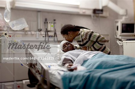 Mother kissing boy in hospital bed with head bandages