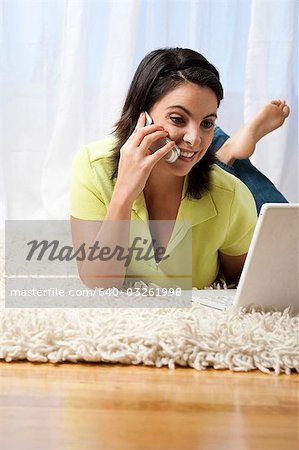 Woman lying down with laptop and cell phone