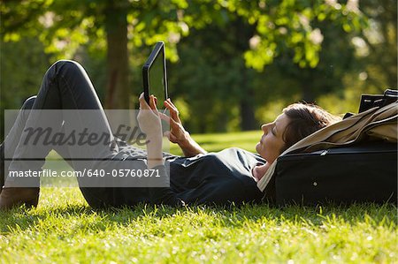 UK, London, Woman lying on grass using tablet