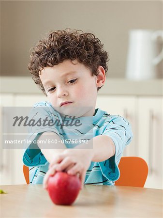 USA, Utah, Boy (6-7) sitting at kitchen table, holding red apple