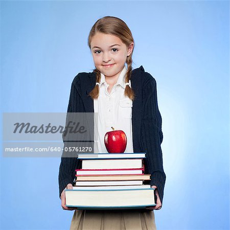 Studio portrait of girl (10-11) holding stack of books and apple
