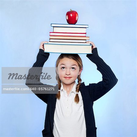 Studio shot of girl (10-11) holding stack of books and apple on head