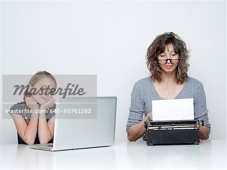 Studio shot of mother using typewriter and daughter (10-11) looking at laptop