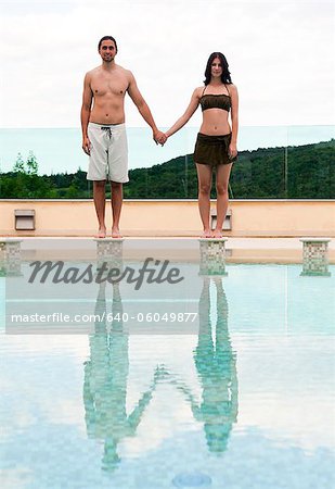 Italy, Tuscany, Couple standing on edge of swimming pool and holding hands