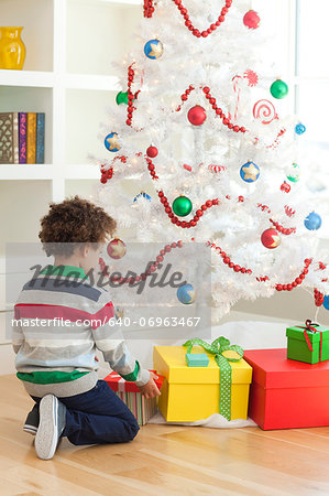 Young boy sitting under Christmas tree, picking up Christmas presents