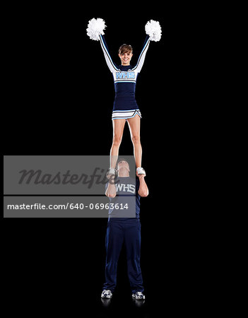 Teenage sportsman(16-17) holding aloft teenage cheerleader girl (16-17)