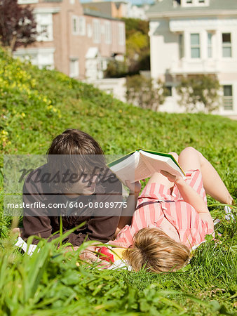 USA,California,San Francisco,Young couple lying on grass reading book