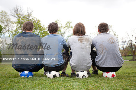 USA, Utah, Provo, Four men sitting on footballs in pitch