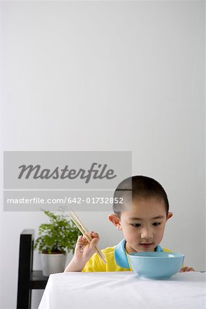 Boy holding chopsticks at dining table, smiling