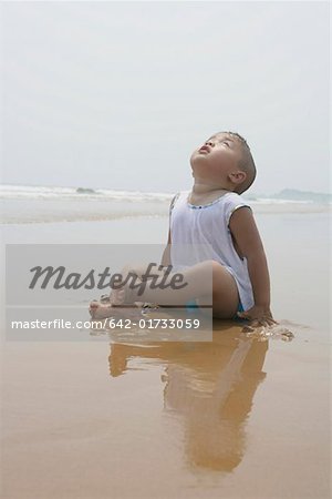 Boy sitting on sand, looking up