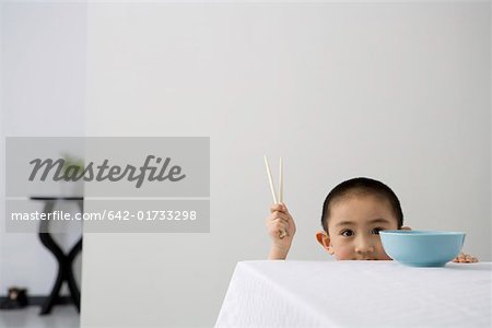 Boy holding chopsticks by table