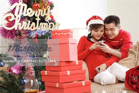 Young couple looking at mobile phone by Christmas tree and gifts