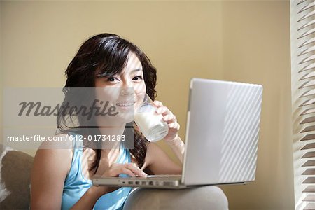 Young woman playing with laptop, drinking milk