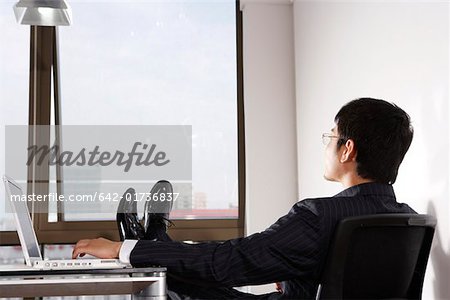 Young man sitting by laptop, rear view