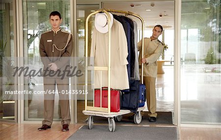 Bellboy delivering luggage to hotel with doorman standing by