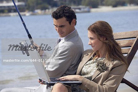 Business couple on beach with fishing rod and laptop