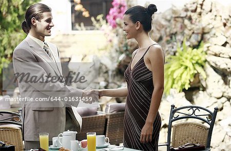 Businessman and businesswoman in garden cafe shaking hands