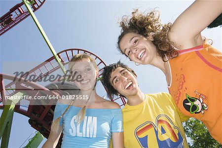 Teenagers posing at roller coaster at amusement park