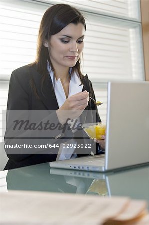 Professional woman eating fruit salad over laptop