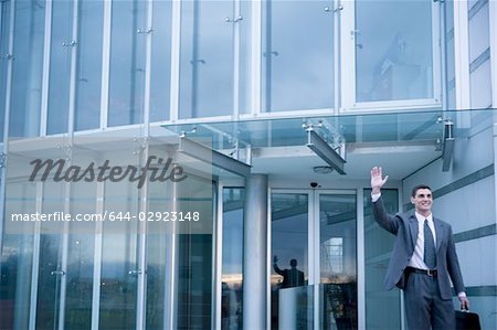 Businessman waving while exiting from office building