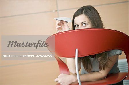 Businesswoman hiding behind chair with paper airplane