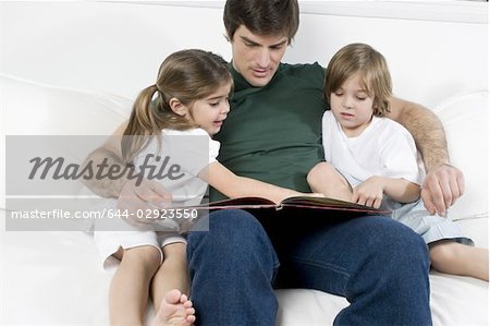 Young man on couch with children reading