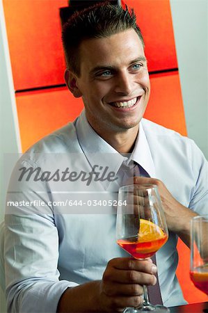 Young man in business attire with glass of orange wine adjusting tie