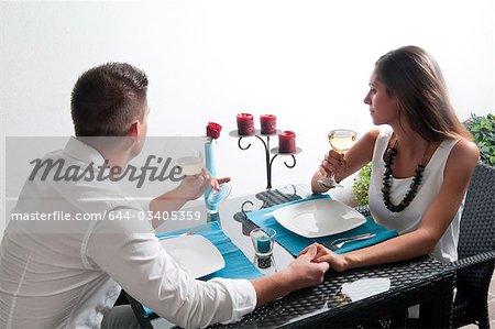 Couple sitting at table drinking white wine and holding hands