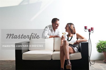 Young man leaning on couch with young woman with book and white wine