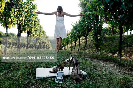 Young woman  in vineyard with high heel shoes, mobile, and laptop in foreground