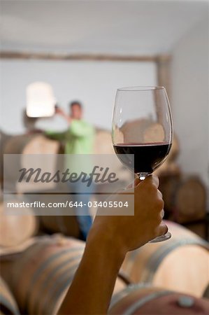 Young woman's hand holding glass of red wine with young man in background