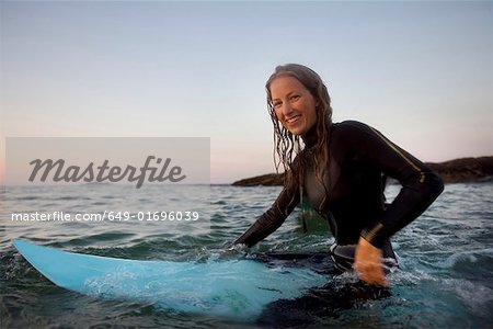 Woman sitting on surfboard in the water smiling.