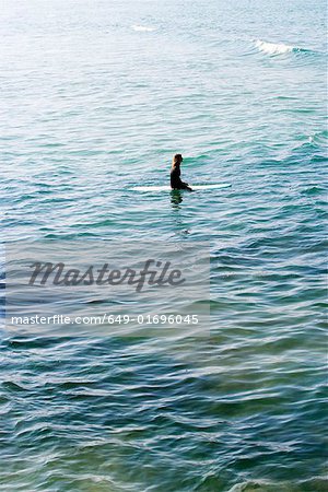 Woman sitting on surfboard in the water.