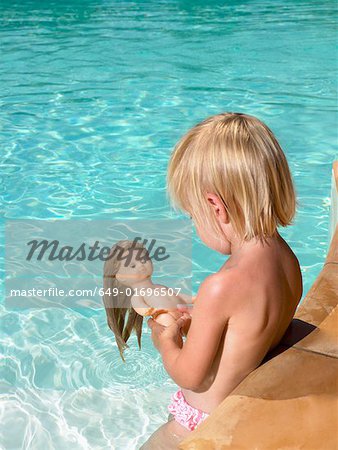 Young boy playing with a doll in a pool.