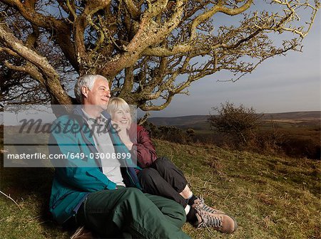 mature couple sitting against tree