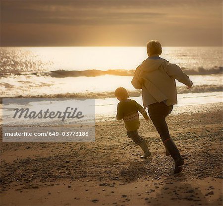 Woman chasing young boy on beach. Autumn