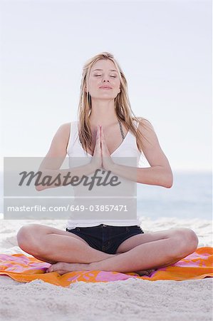 Woman meditating on towel at beach